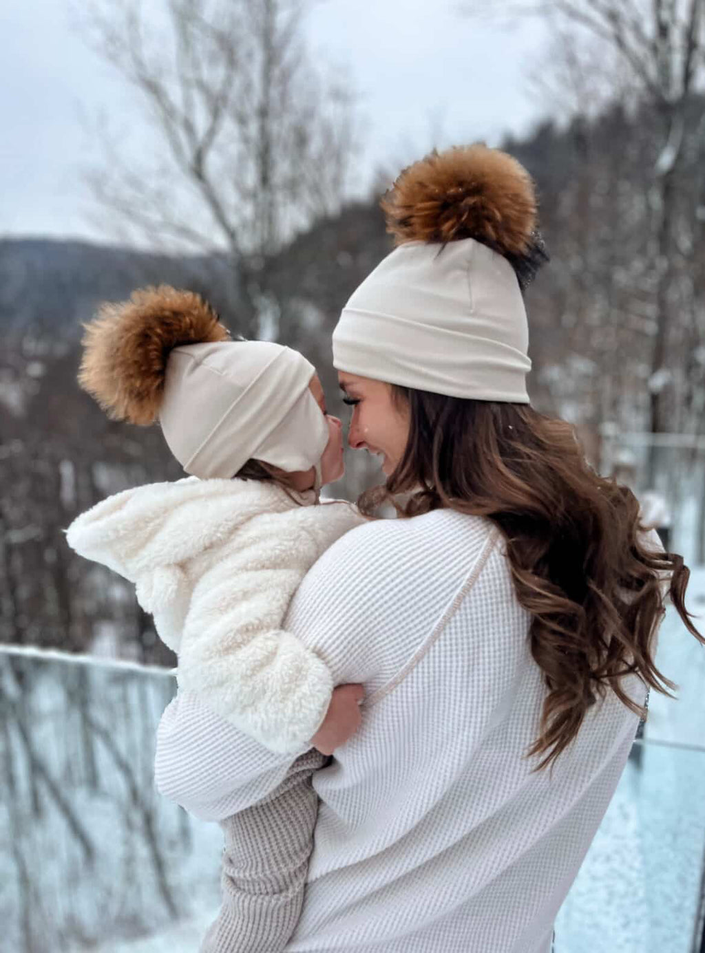 Maman et bébé se donnant un bisou dehors dans la neige avec leurs tuques Kplla Canada