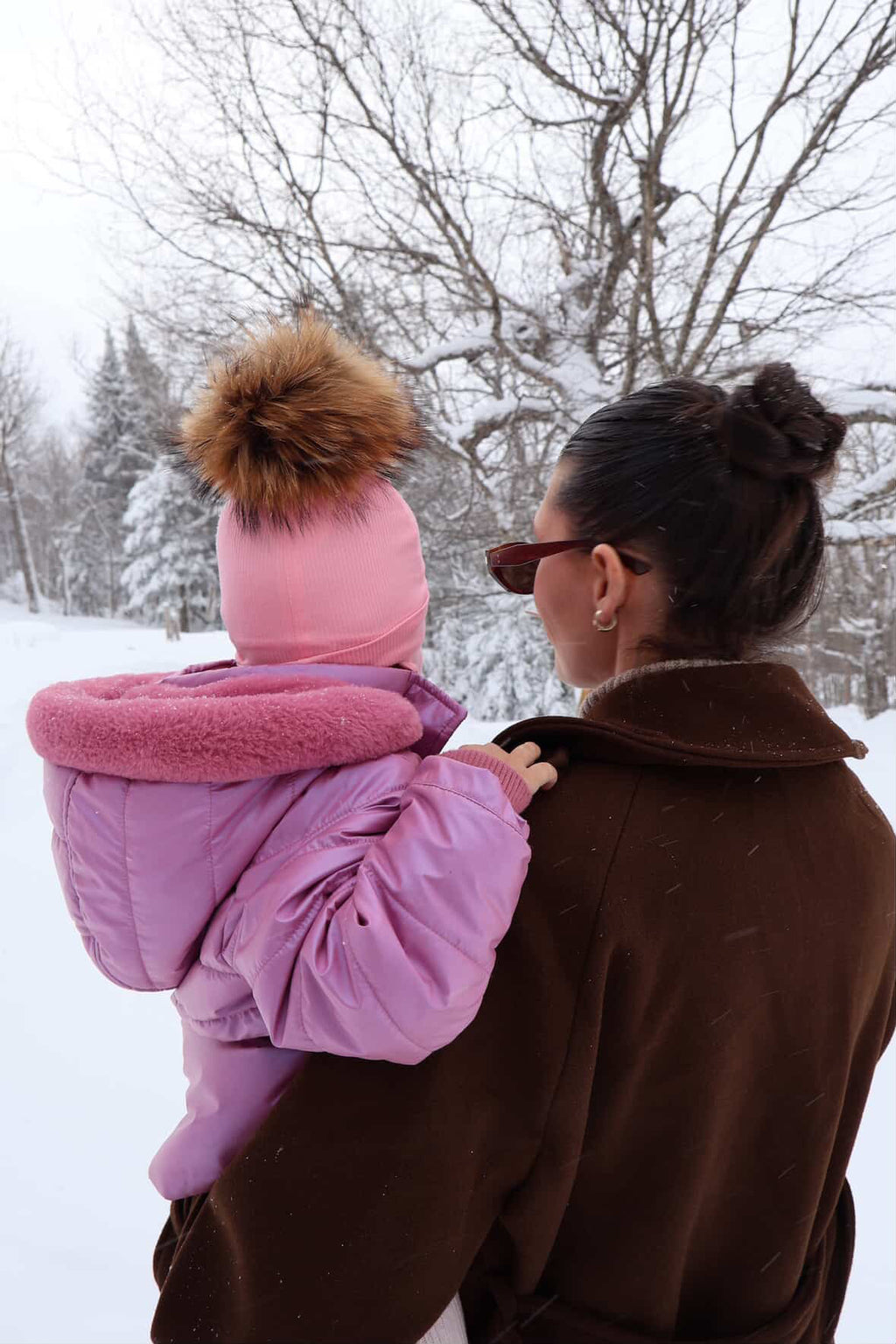 Tuque bébé rose Kplla avec pompon portée en hiver dans les bras de sa maman