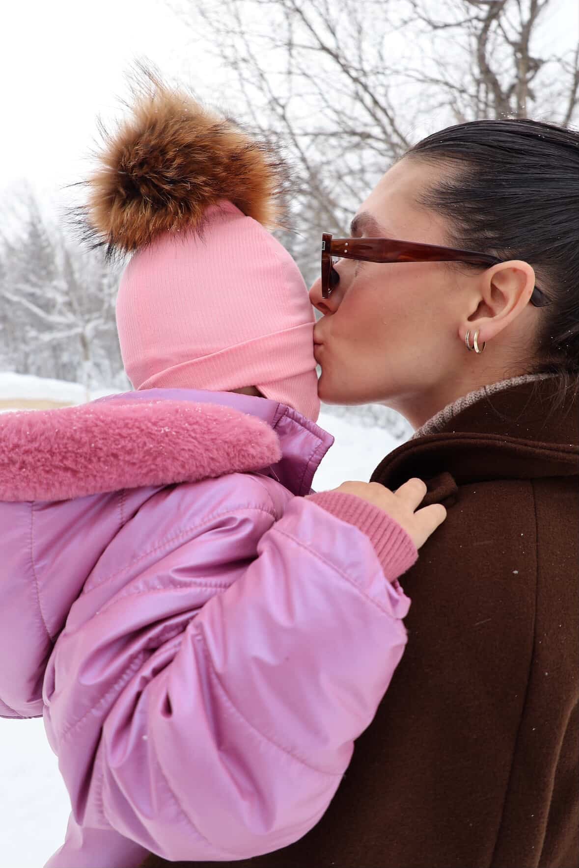 Bébé avec tuque rose Kplla avec pompon dans les bras de sa maman en hiver