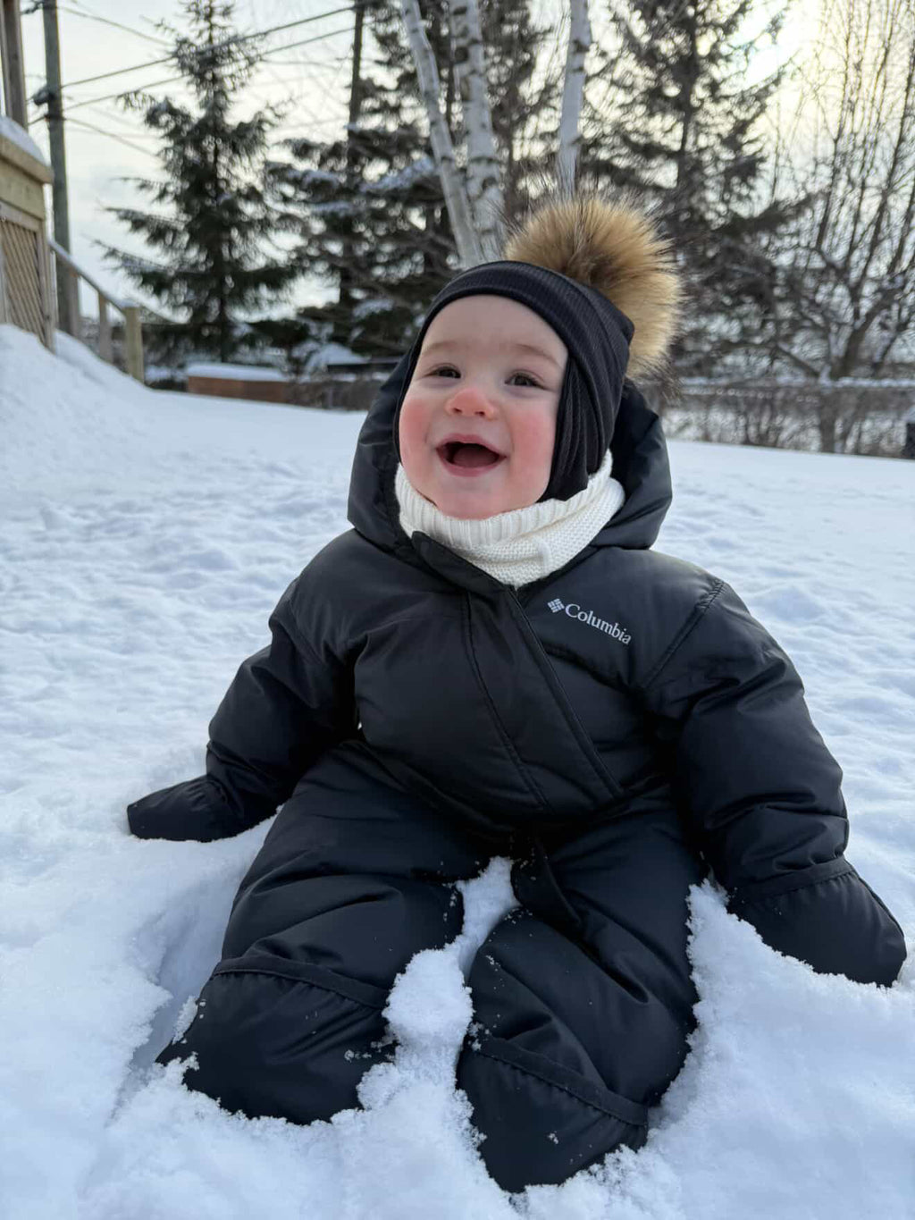 Bébé portant une tuque noire Kplla avec pompon dans la neige
